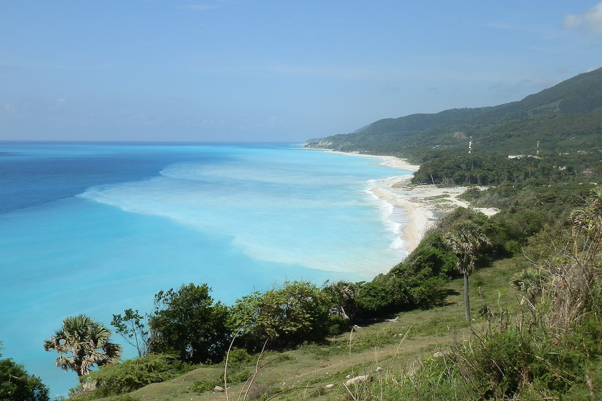 El Caribe a los pies de Bahoruco
La sierra de Bahoruco, al Suroeste de Rep&uacute;blica Dominicana, es un macizo monta&ntilde;oso de 2200 metros de altura que se encuentra con el Caribe con grandes acantilados que alternan con ensenadas donde desembocan los r&iacute;os que evacuan las aguas de este gran sistema k&aacute;rstico tropical. Las aguas turquesas del caribe reciben una pluma de sedimento blanquecina de las fuertes lluvias del d&iacute;a anterior, avenado por manantiales y sorteado de cavidades y cascadas de tobas travert&iacute;nicas. La Playa de San rafael, abajo, es un lugar de esparcimiento popular dominicano, lejos del turismo internacional. La sierra de Bahoruco posee un rico sistema de vegetaci&oacute;n que conforma una cliserie que de abajo a arriba va desde las selvas h&uacute;medas al este&nbsp; y los bosques secos al sur y norte, a las selvas nubladas a media altura y coronando los pinares tropicales. En esta sierra se ocult&oacute; y luch&oacute; contra los espa&ntilde;oles en el siglo XVI uno de los grandes h&eacute;roes simb&oacute;licos del pa&iacute;s, el cacique Enriquillo. Al final el emperador Carlos I, por delegaci&oacute;n, tuvo que firmar un tratado de paz con &eacute;l, reconociendo el derecho a los ind&iacute;genas tainos que quedaba instalarse en la que ser&iacute;a la nueva poblaci&oacute;n de Azua.